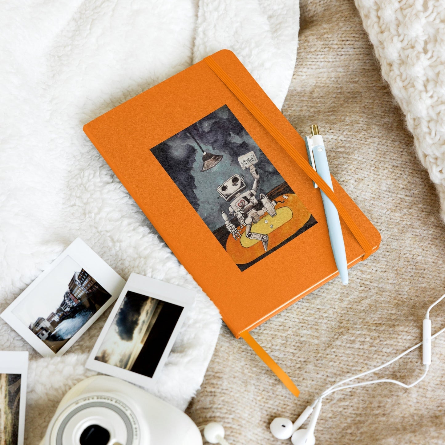 Hardcover notebook with orange UltraHyde cover, elastic closure, and ribbon marker, surrounded by photos and a pen.